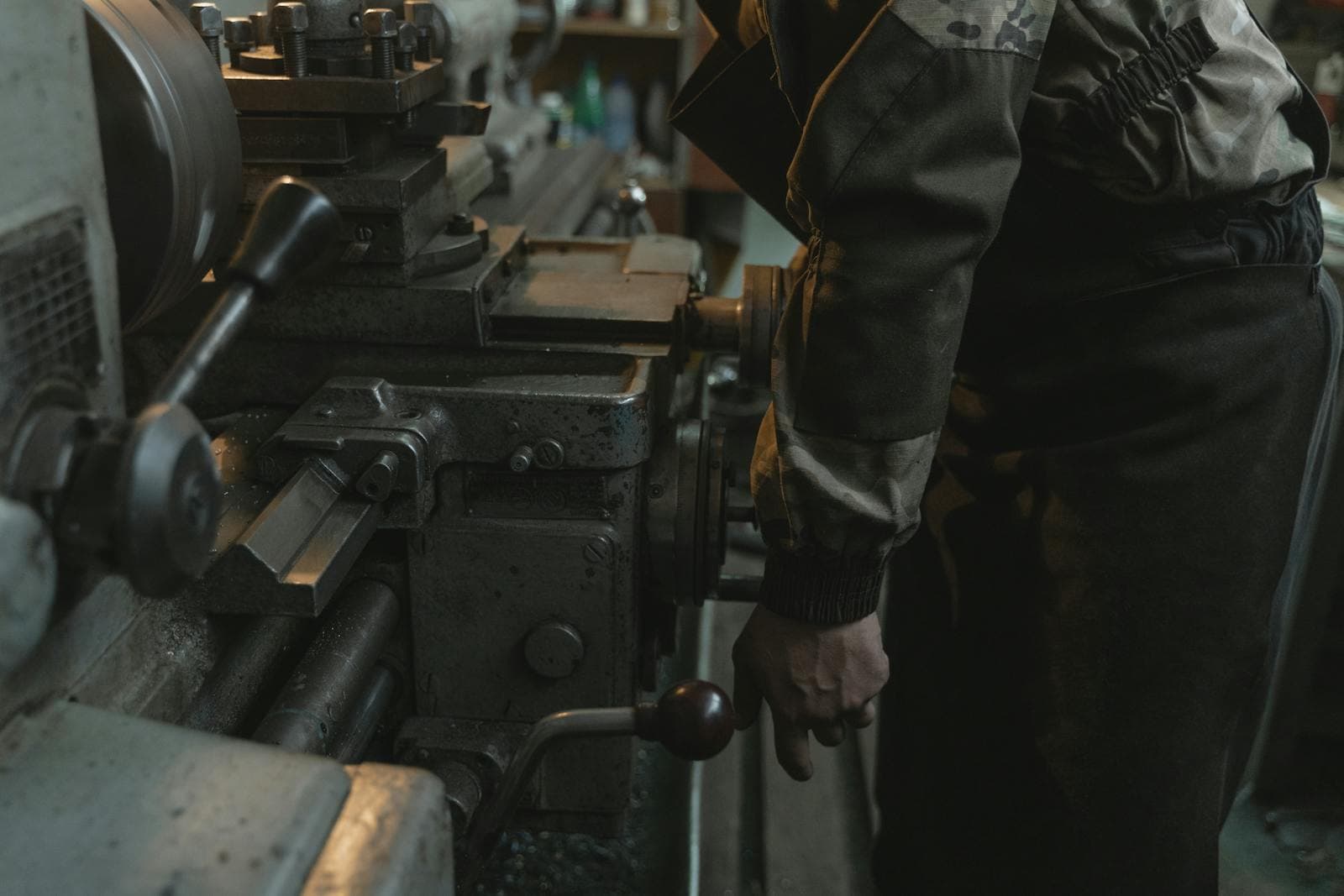 Machinist operating a manual lathe in a workshop, hand on the carriage handwheel
