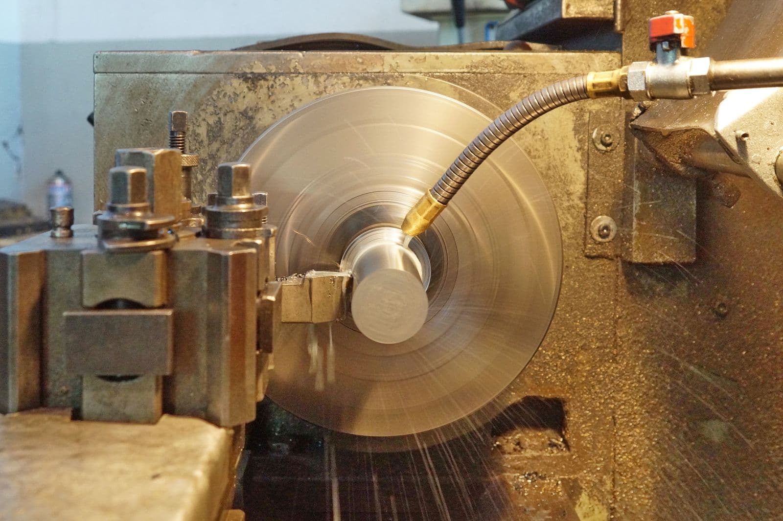 Manual lathe turning a steel part with a coolant nozzle directed at the cutting zone
